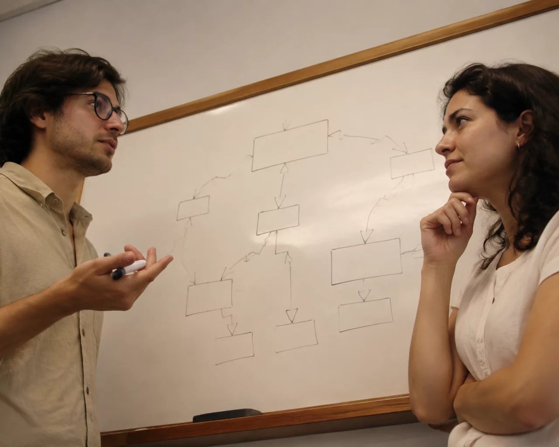 Duas pessoas em pé diante de um quadro branco onde um argumento está desenhado