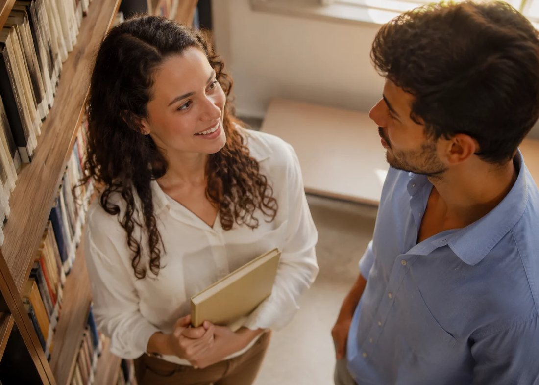 Participantes conversando em pé no corredor entre estantes de livros altas